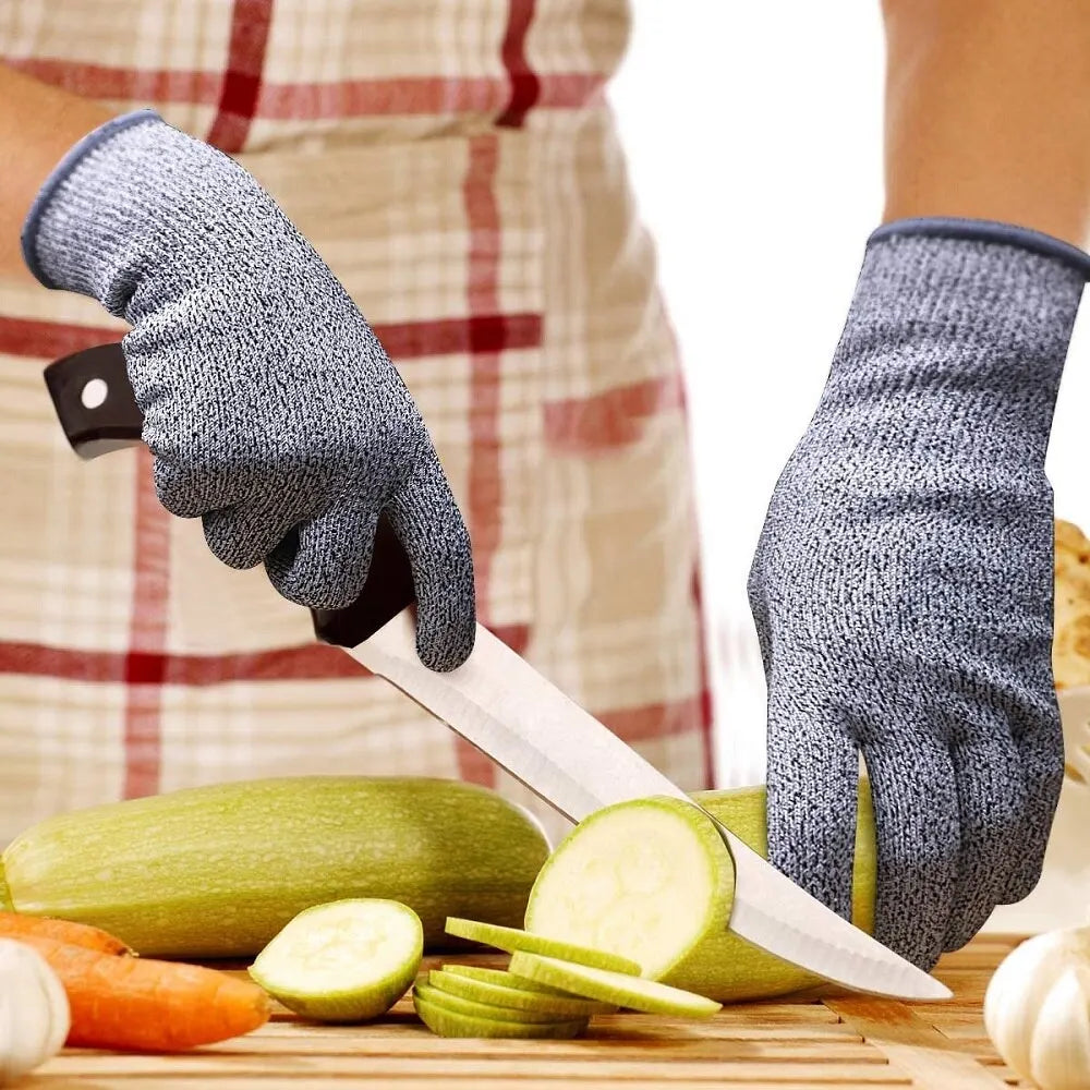 Grey cut-resistant safety gloves being worn while slicing zucchini with a kitchen knife on a cutting board.