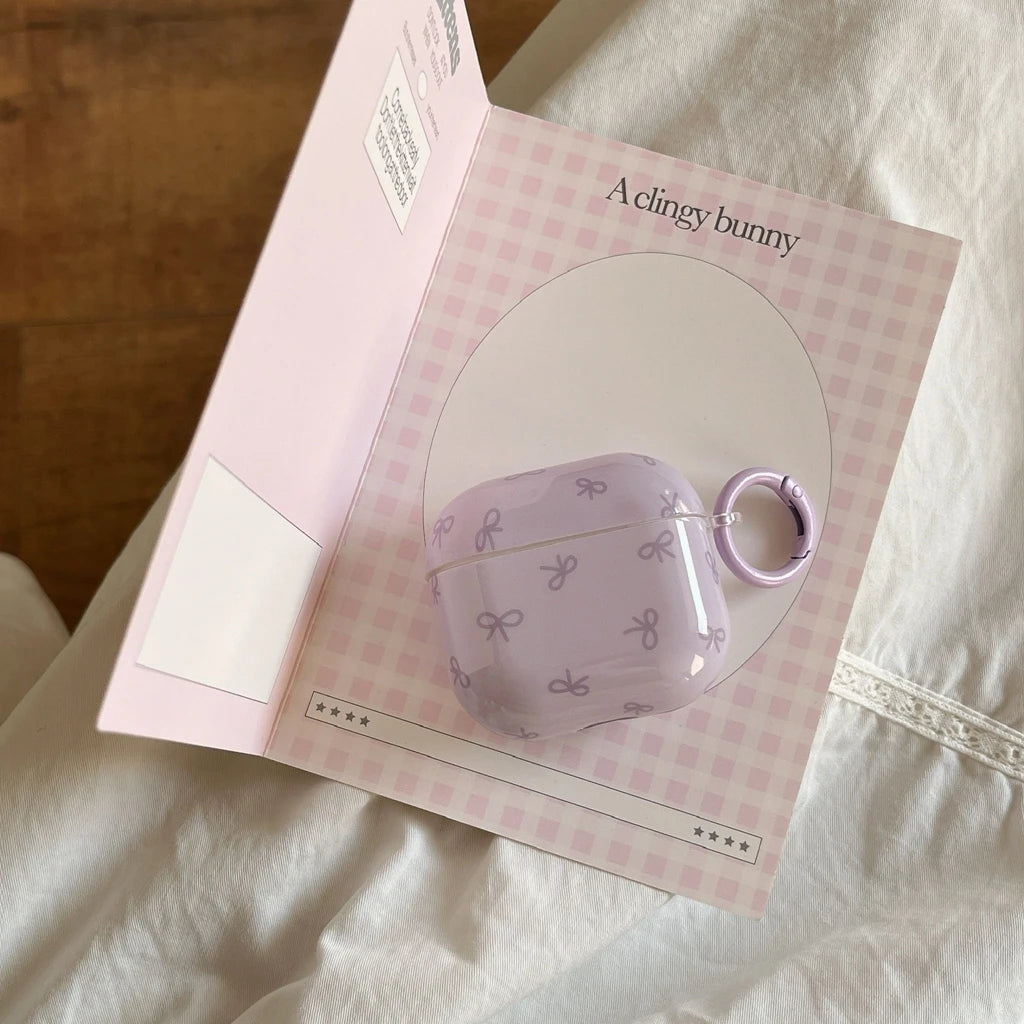 Glossy lilac AirPods case with small bow pattern and matching keyring, in 'A clingy bunny' branded packaging.