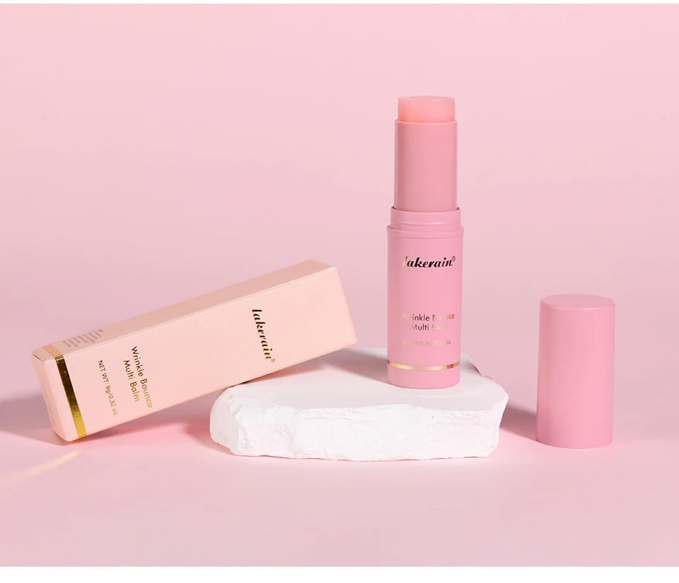 Pink wrinkle bounce multi-balm stick with its box, standing on a white stone base against a soft pink background.