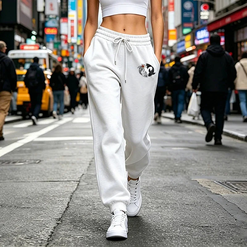 White joggers with a drawstring waist and black-and-white koi fish graphic on the hip, worn with white sneakers.