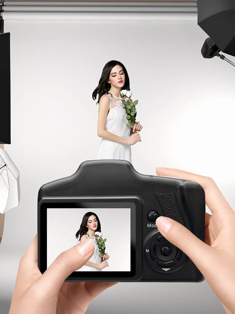 Black plastic digital camera held by hands, showing a live photo preview of a woman in a white dress on the screen.
