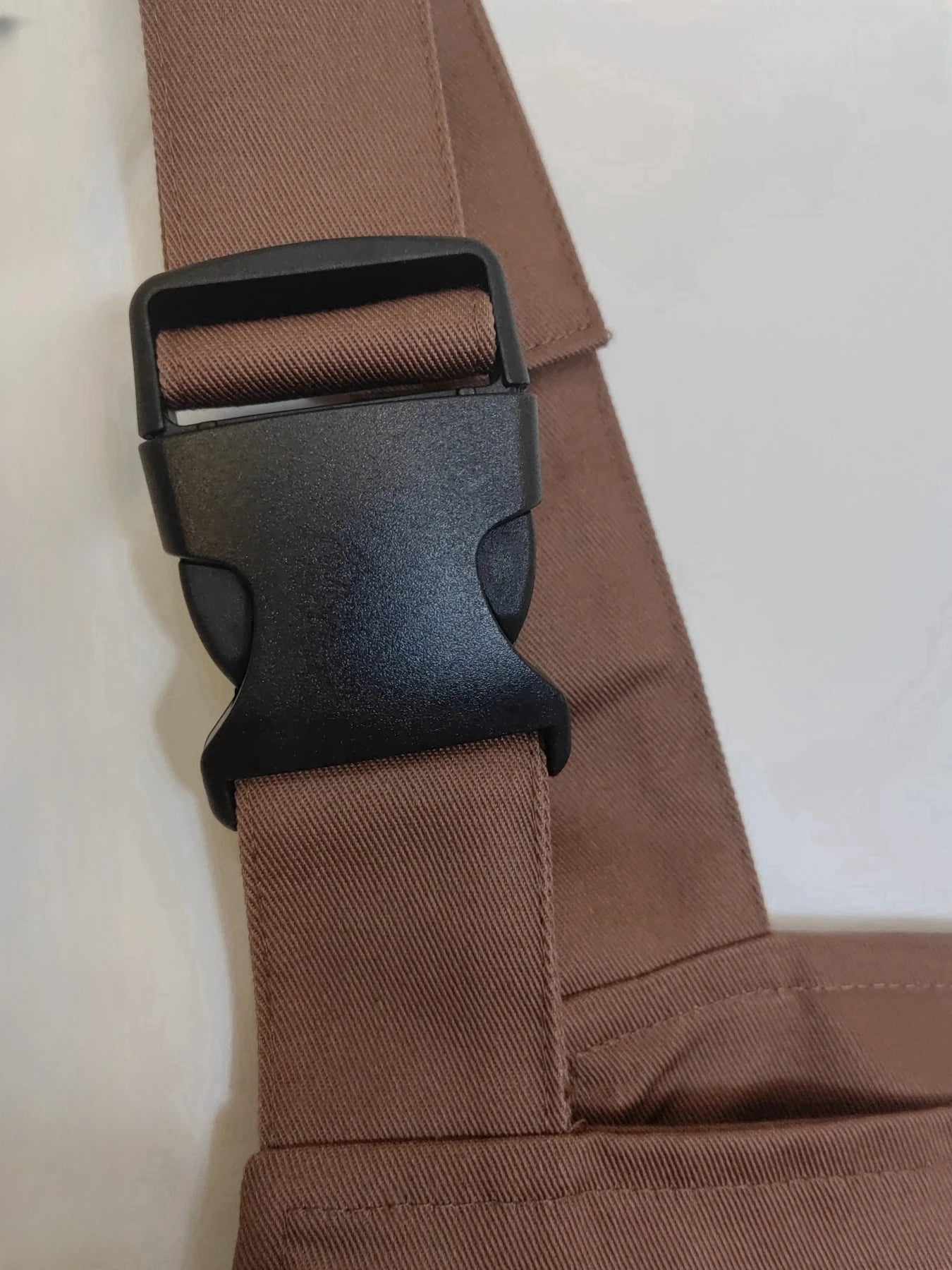 Close-up of a brown, heavy-duty workshop coverall strap featuring a durable black plastic side-release buckle.