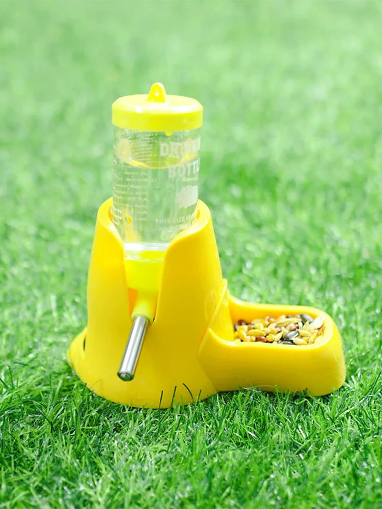 Bright yellow pet feeder and water bottle combo with a metal nozzle, sitting on green grass.
