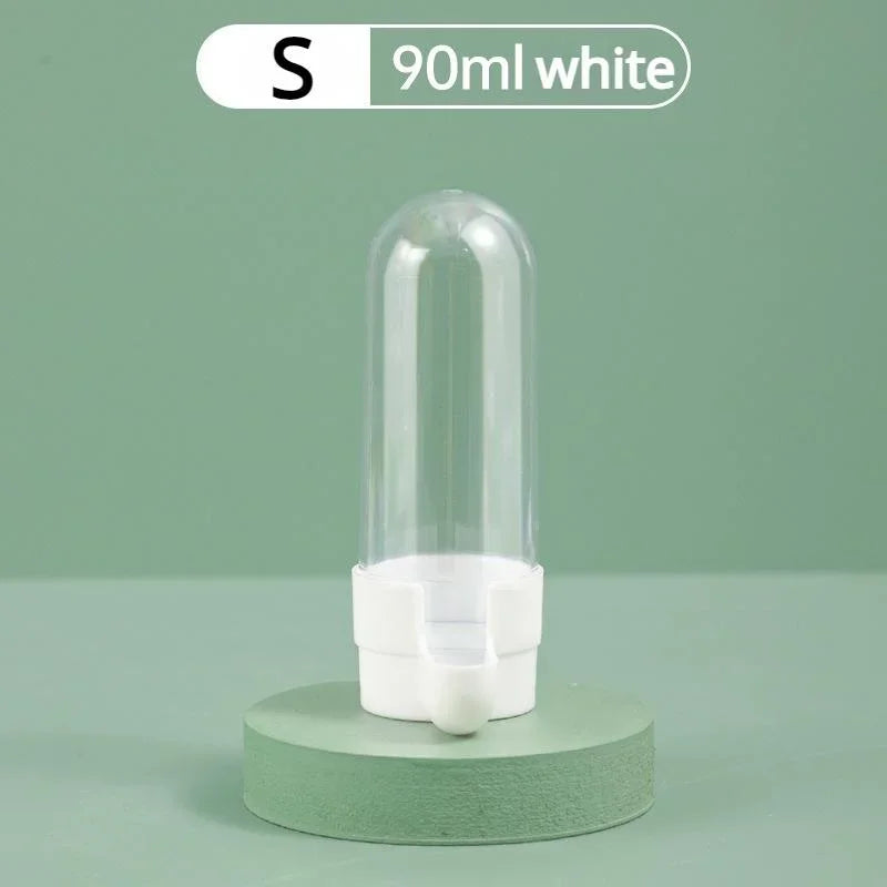 A 90ml clear plastic bird water dispenser with a white base, standing on a green circular pedestal.
