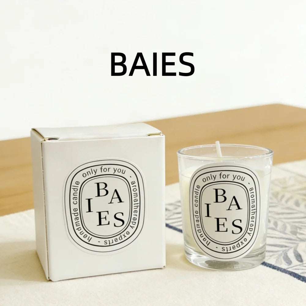 Scented candle in a clear glass jar and matching white gift box, both with an oval “BAIES” label, on a table.
