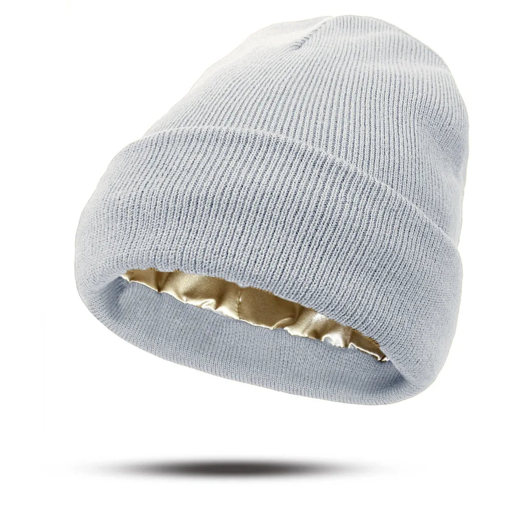 A light grey knitted beanie hat with a luxurious gold satin lining and a folded cuff.