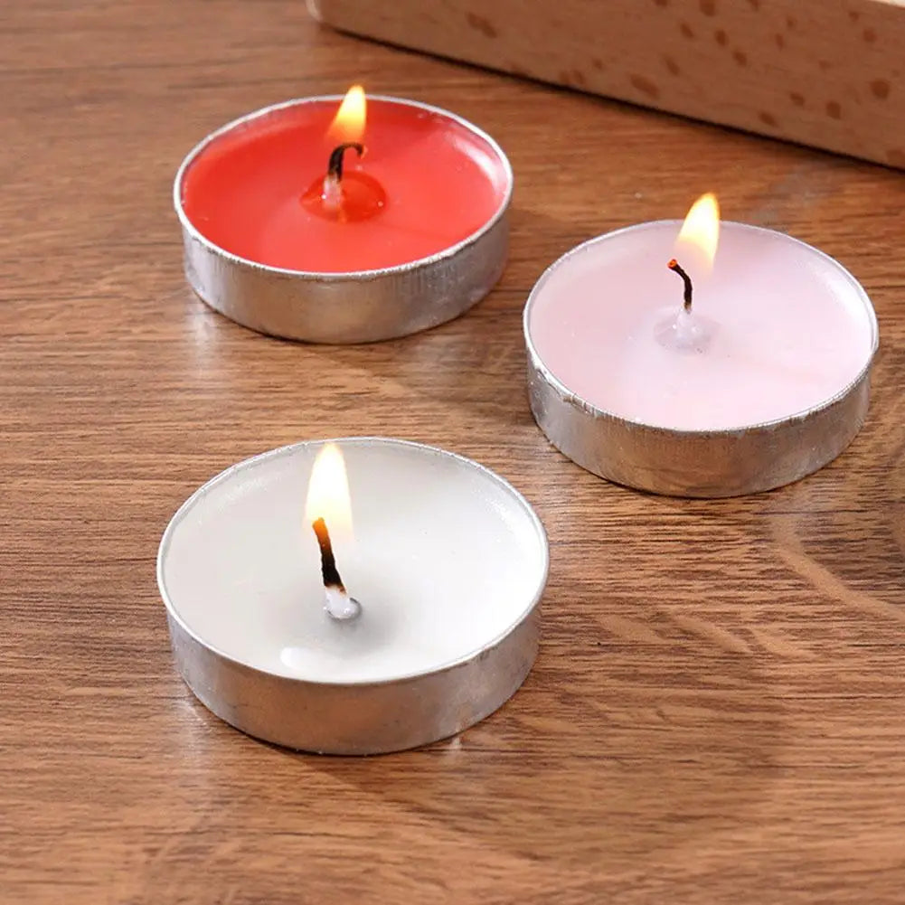 Three lit tea light candles in red, pink, and white wax, each in a small round metal holder on a wooden surface.