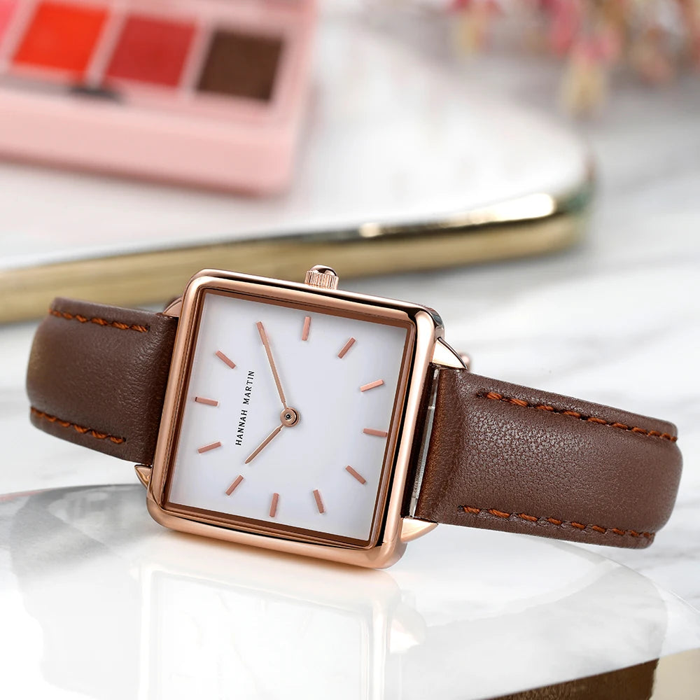 Rose gold square watch with a white face, minimalist markers, and a brown leather strap.