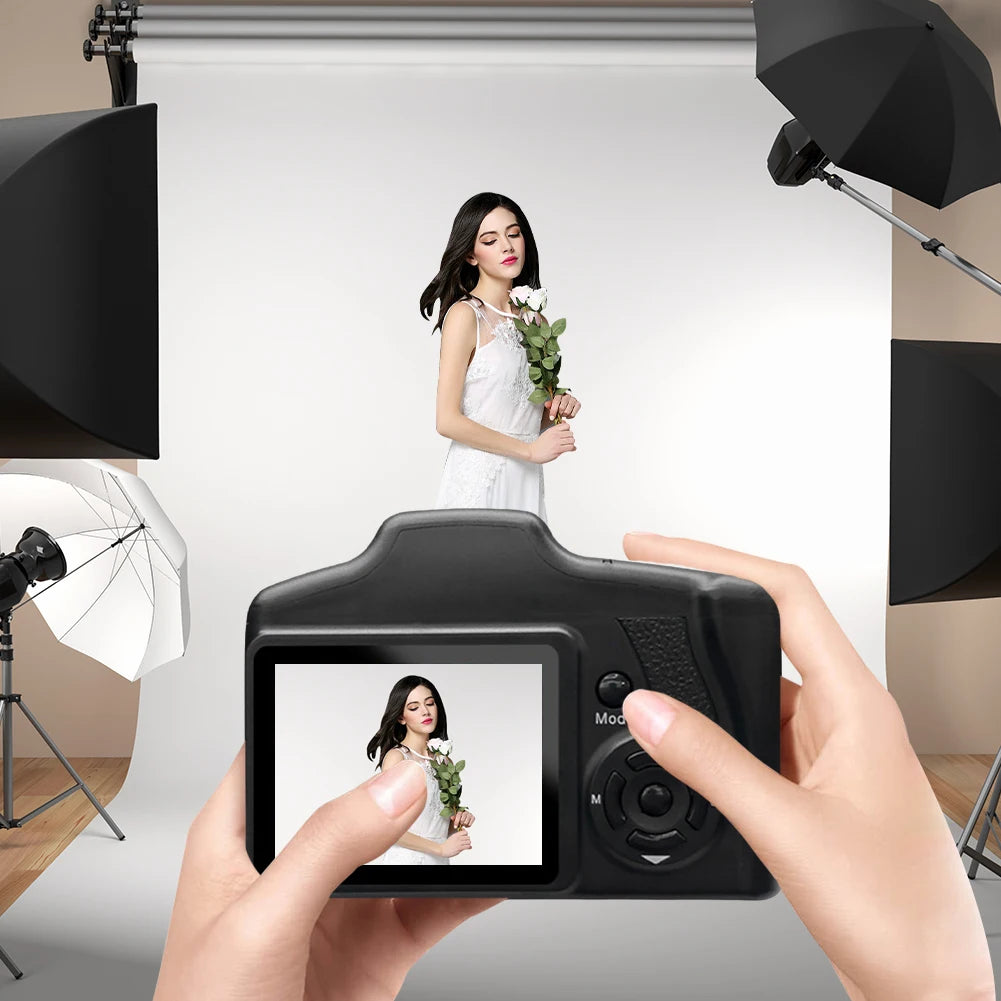 Hands holding a black digital camera with a screen showing a woman in a white dress in a photography studio.