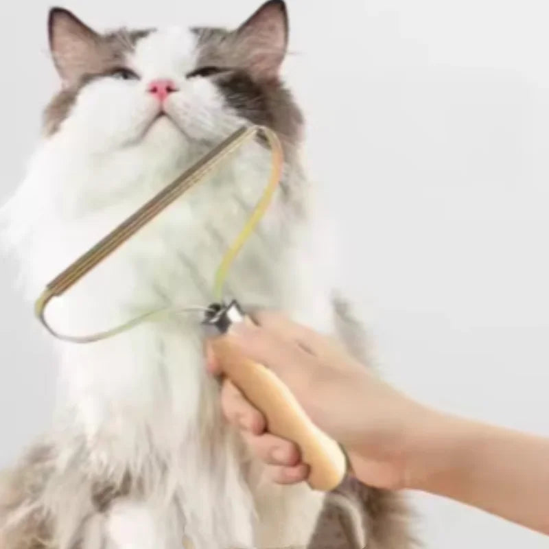 A hand using a gold-coloured metal lint remover with a wooden handle to groom a fluffy grey and white cat.