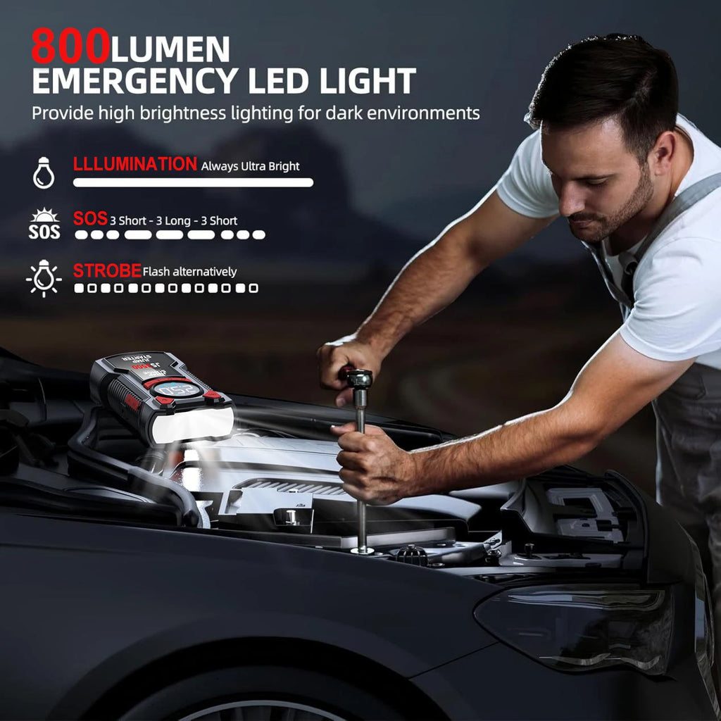 Black jump starter and air compressor resting under a car hood, illuminating the engine with its bright LED flashlight.