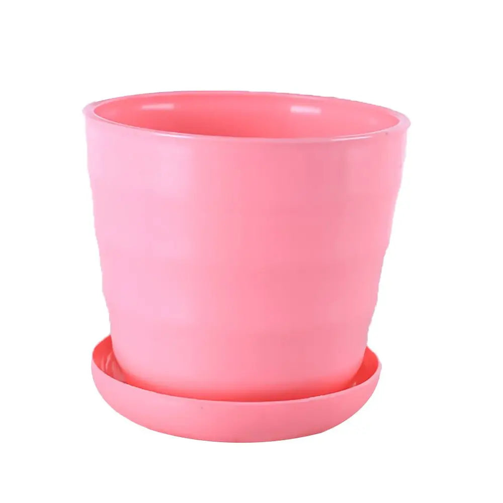 A smooth, light pink plastic flower pot with a matching saucer, featuring a subtle horizontal ribbed design.