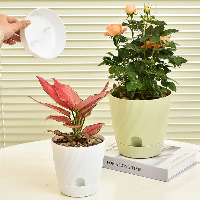 Two minimalist, swirling plastic pots in white and pale green, each housing a plant, with a matching removable base.