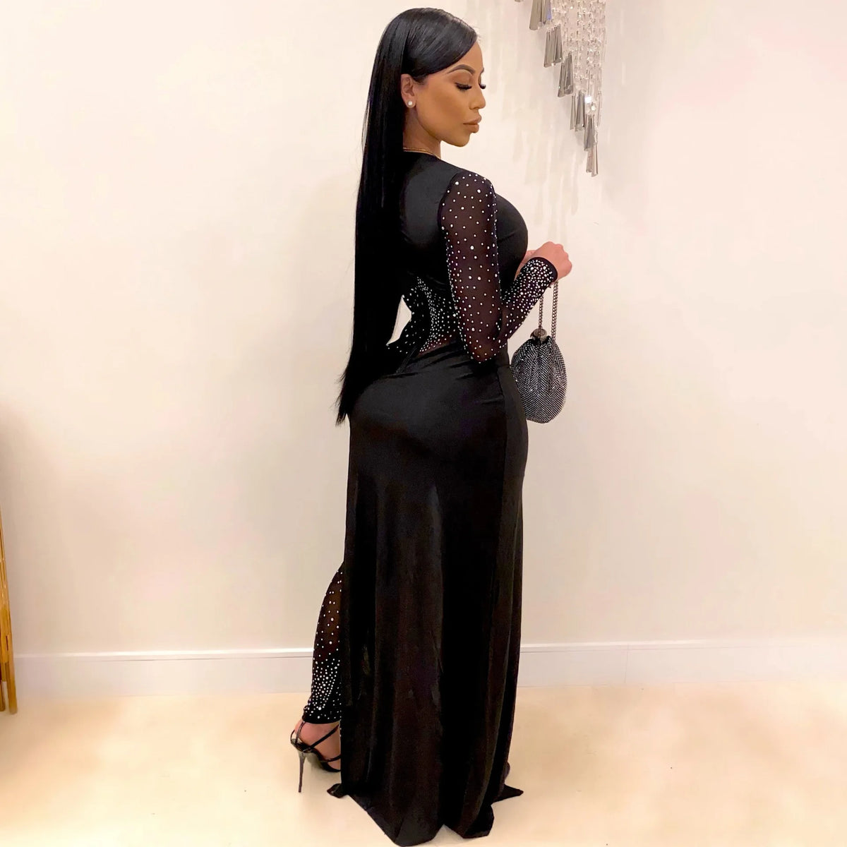 Woman wearing a black long-sleeve skinny jumpsuit with sheer mesh patchwork and rhinestone embellishments.