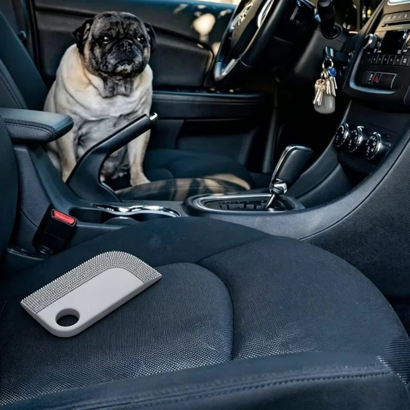 Grey silicone pet hair remover tool on a black car seat, with a pug sitting in the passenger seat.