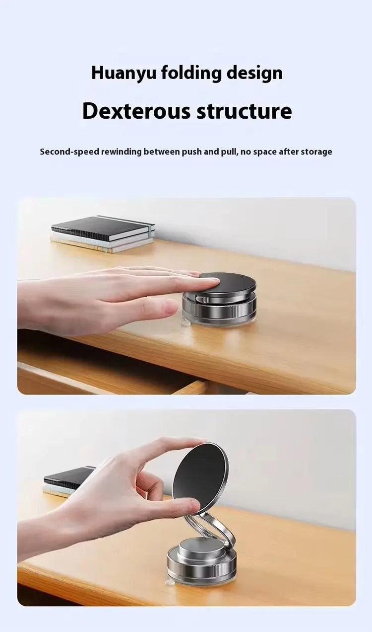 A compact, circular metallic folding stand with a black surface being adjusted by a hand on a wooden desk.