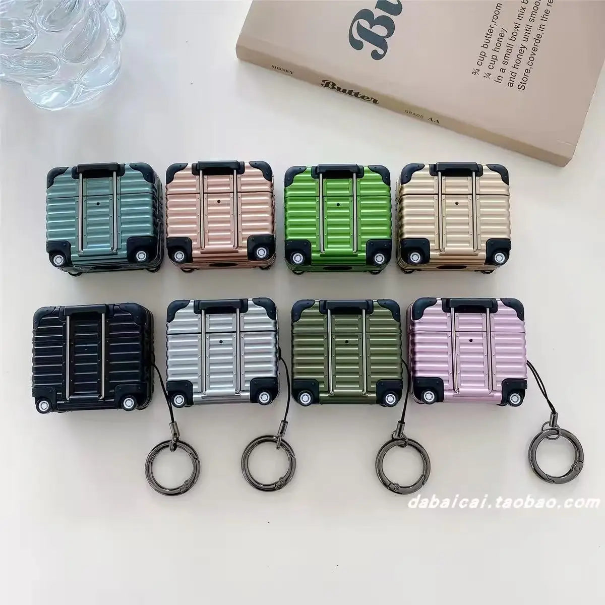 Multi-coloured, hard-shell suitcase style protective cases for AirPods, featuring a metal keychain attachment.