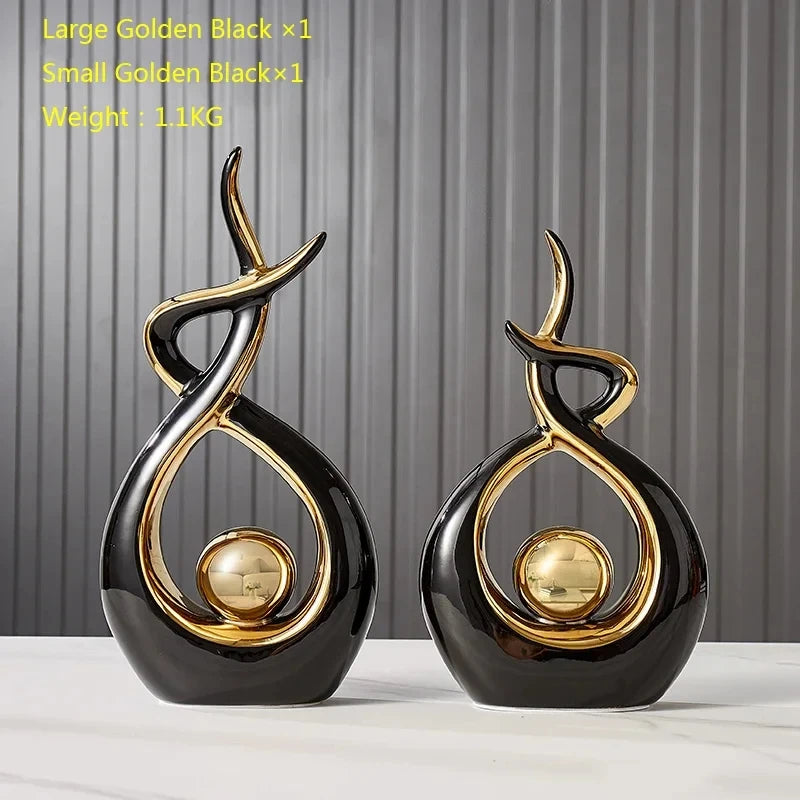Set of two sleek, black and gold ceramic abstract figurines with a curved, flame-like design and central gold sphere.