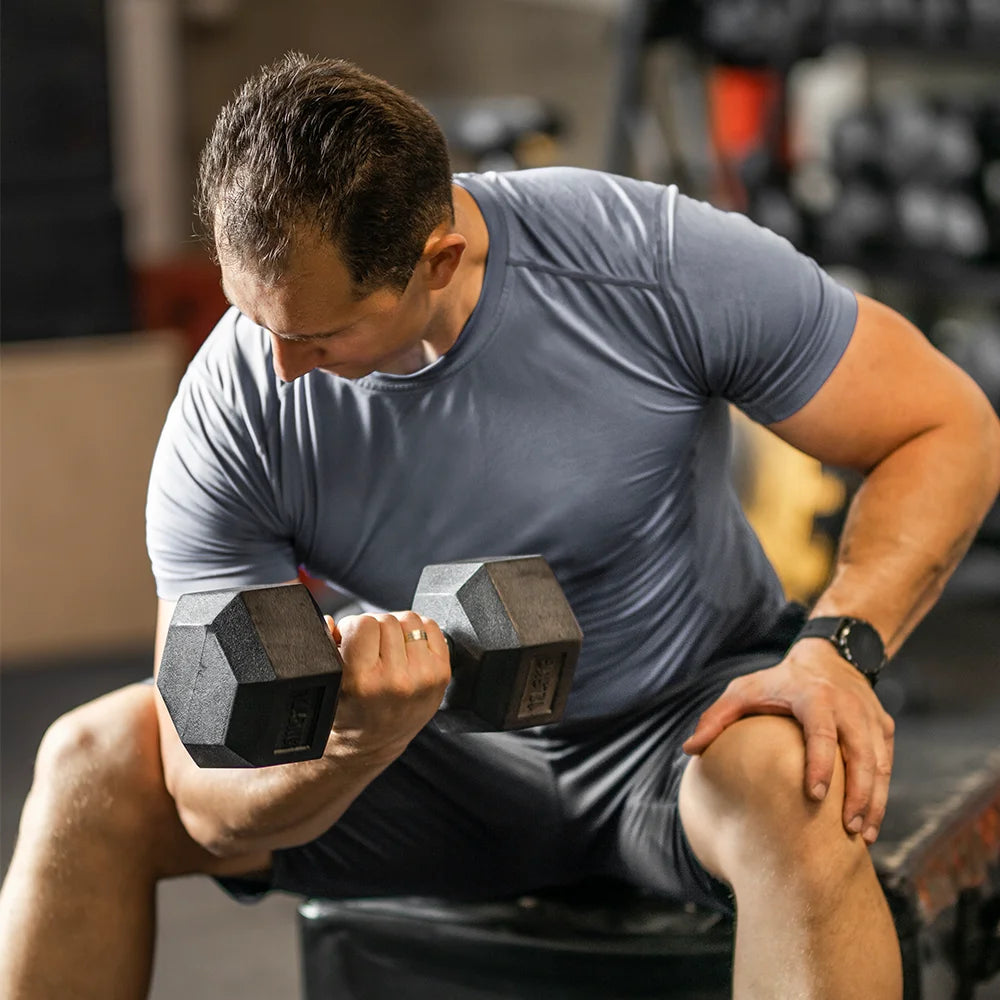 A man sitting on a bench lifts a black hexagonal dumbbell.