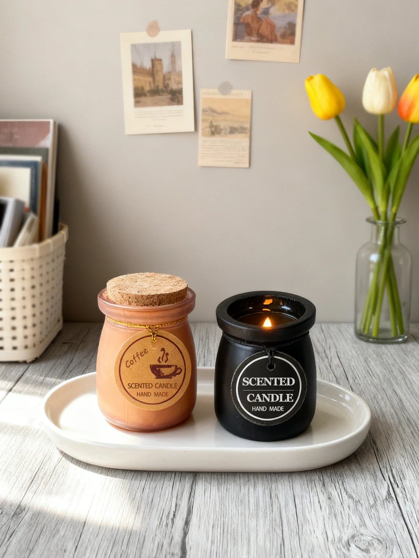 Two handmade scented candles in black and coffee-coloured glass jars, on a white tray with a lit wick and cork lid.