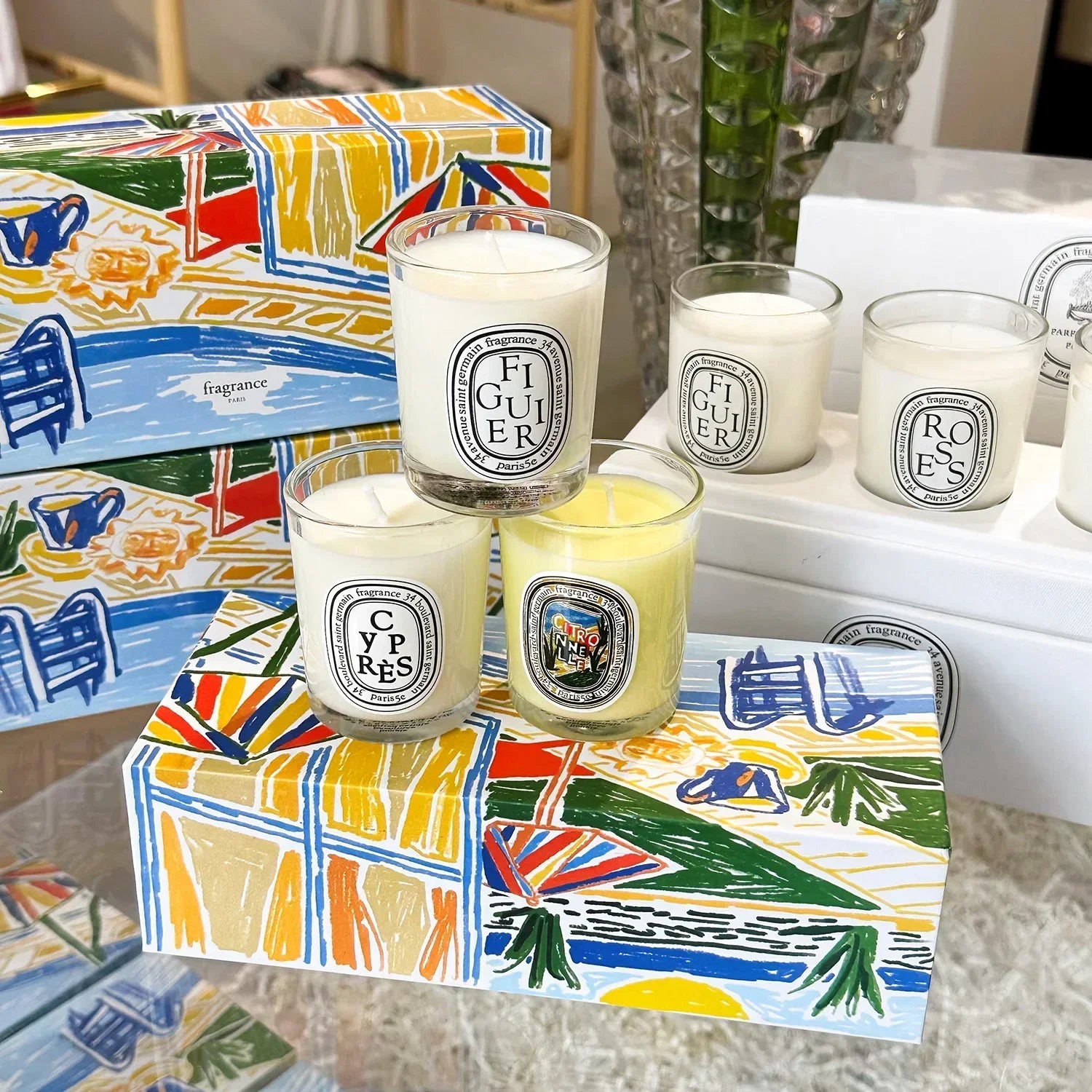 Set of scented candles in clear glass jars, displayed on colourful, artistic summer-themed gift boxes.