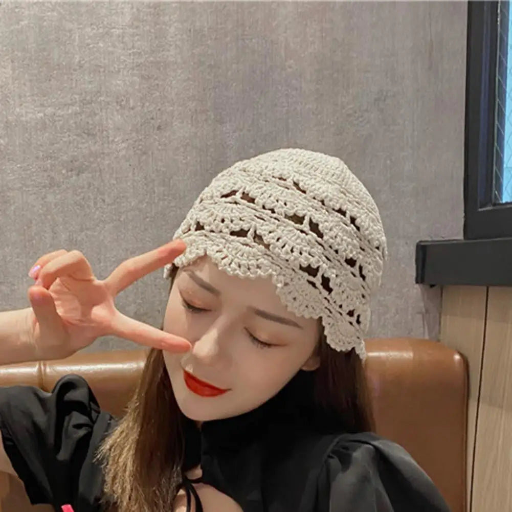 A woman wearing a cream, hollow-patterned crochet beanie with a delicate scalloped edge.