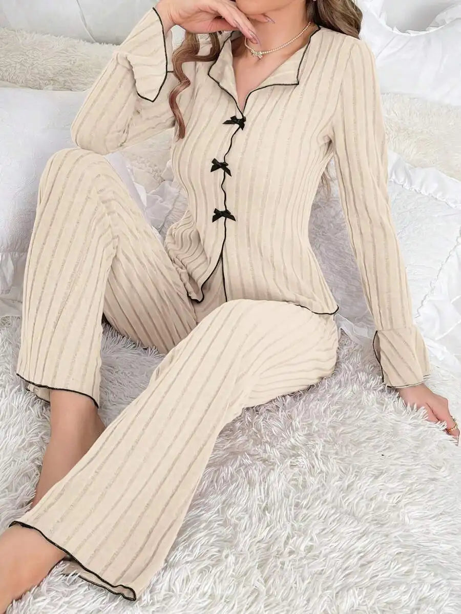 Beige ribbed loungewear set with black piping, button-up top with bow detailing, and matching wide-leg trousers.