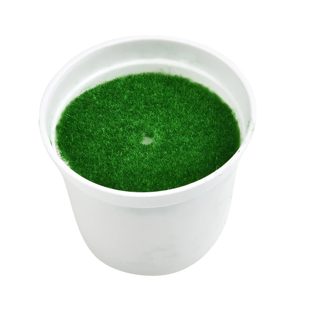 A plain white plastic plant pot filled with artificial green grass, isolated against a white background.