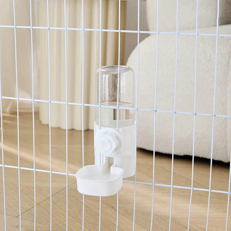 Clear plastic pet water dispenser with a white mount, attached to a white wire cage.