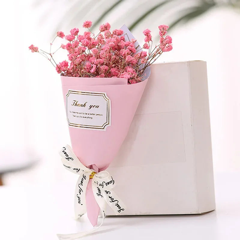 A bouquet of pink gypsophila flowers in pink wrapping with a 'Thank you' label and decorative ribbon next to a box.