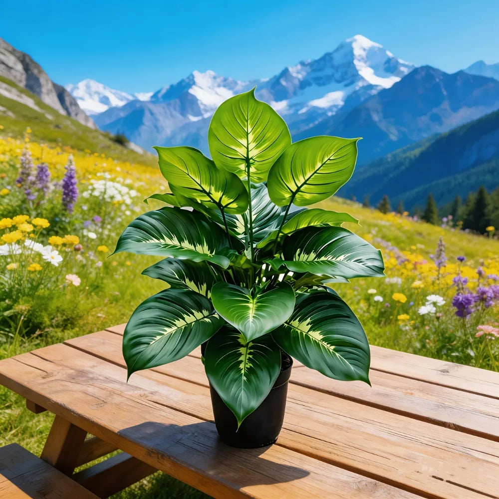 Artificial plant with large, pointed green and cream leaves in a black pot on a wooden table, snowy mountains background.