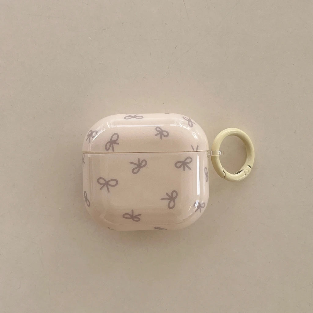 Cream glossy AirPods case with purple bow pattern and yellow keychain ring. Compatible with AirPods.