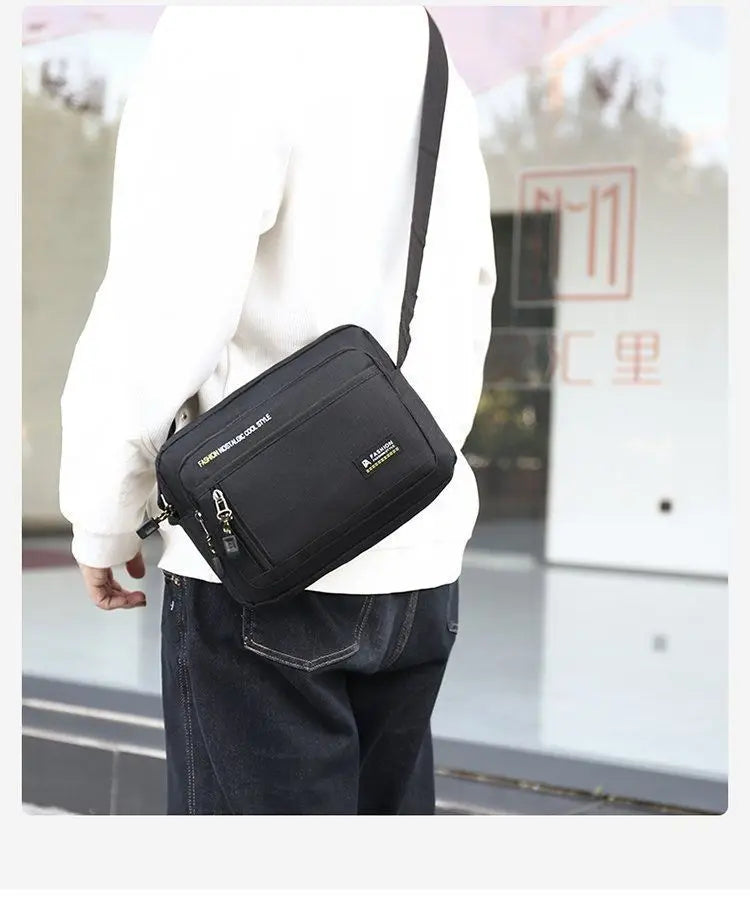 A man wearing a black, rectangular crossbody bag with an adjustable shoulder strap and zip pockets.