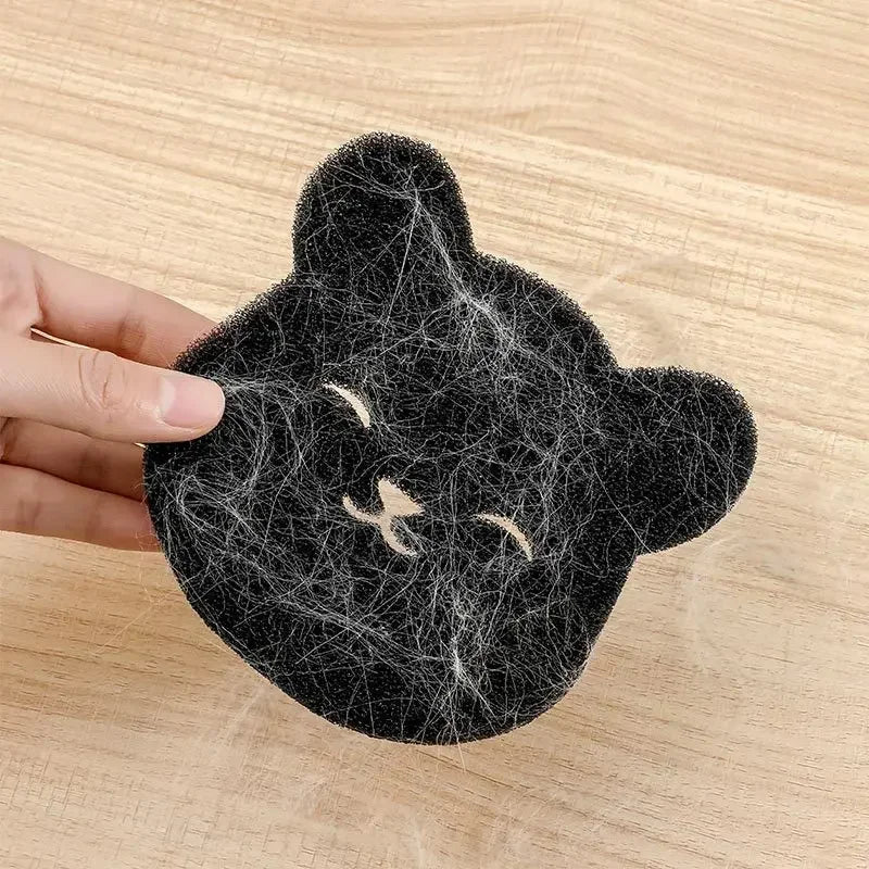 A black bear-shaped pet hair remover sponge with light-coloured hair caught on its surface, held by a hand.