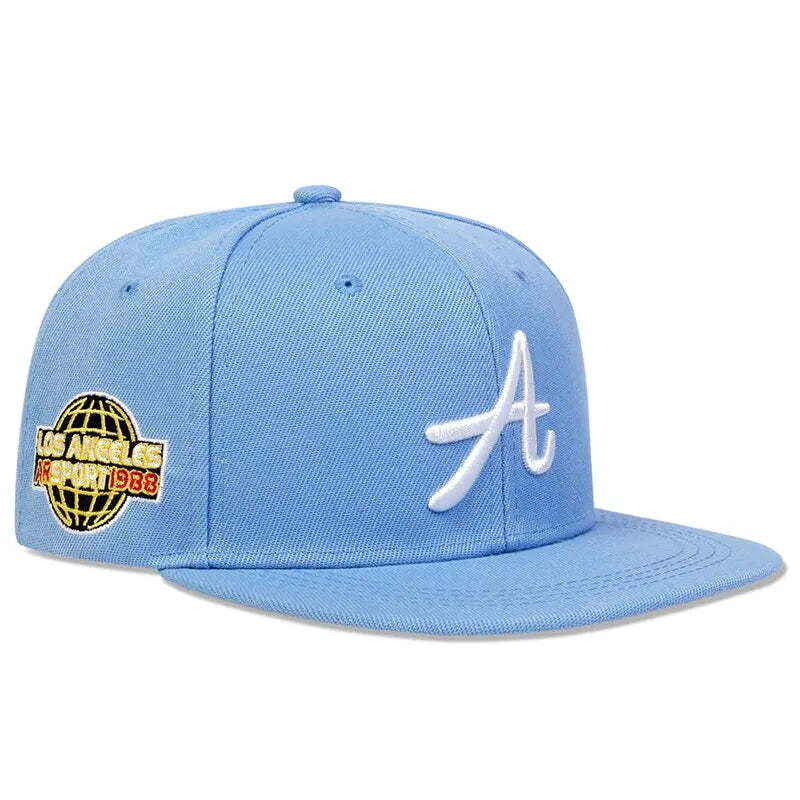 Light blue flat-peak baseball cap with white embroidered letter 'A' and Los Angeles globe patch on the side.
