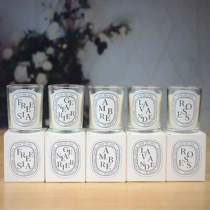 Five luxury scented candles in glass jars with white, minimalist labels and matching presentation boxes.
