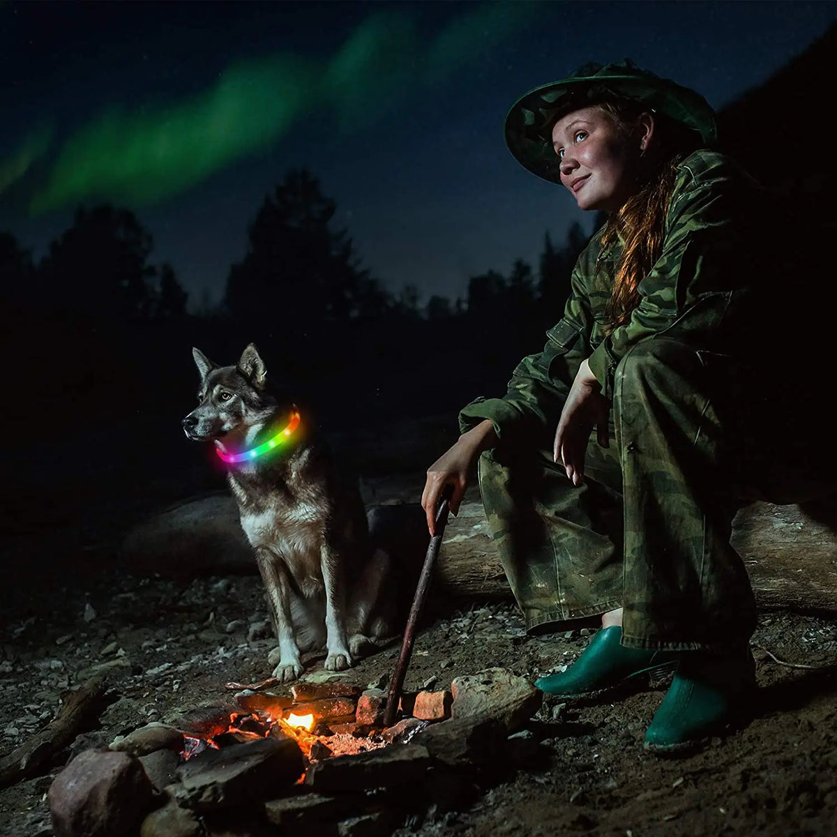 Multi-colored glowing silicone LED dog collar worn by a dog sitting by a campfire with its owner.