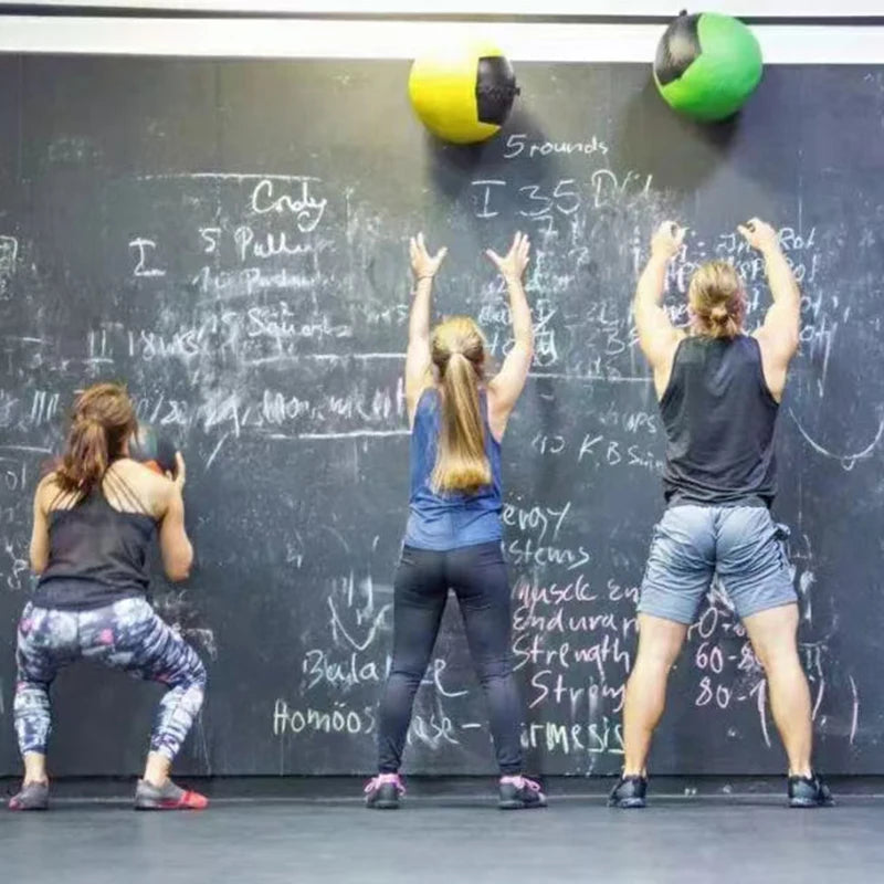 Three people facing a chalk-covered wall, throwing medicine balls in a gym.