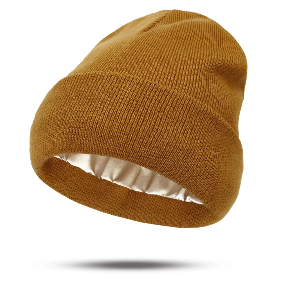A mustard-yellow knitted beanie hat with a smooth, cream-coloured satin lining.