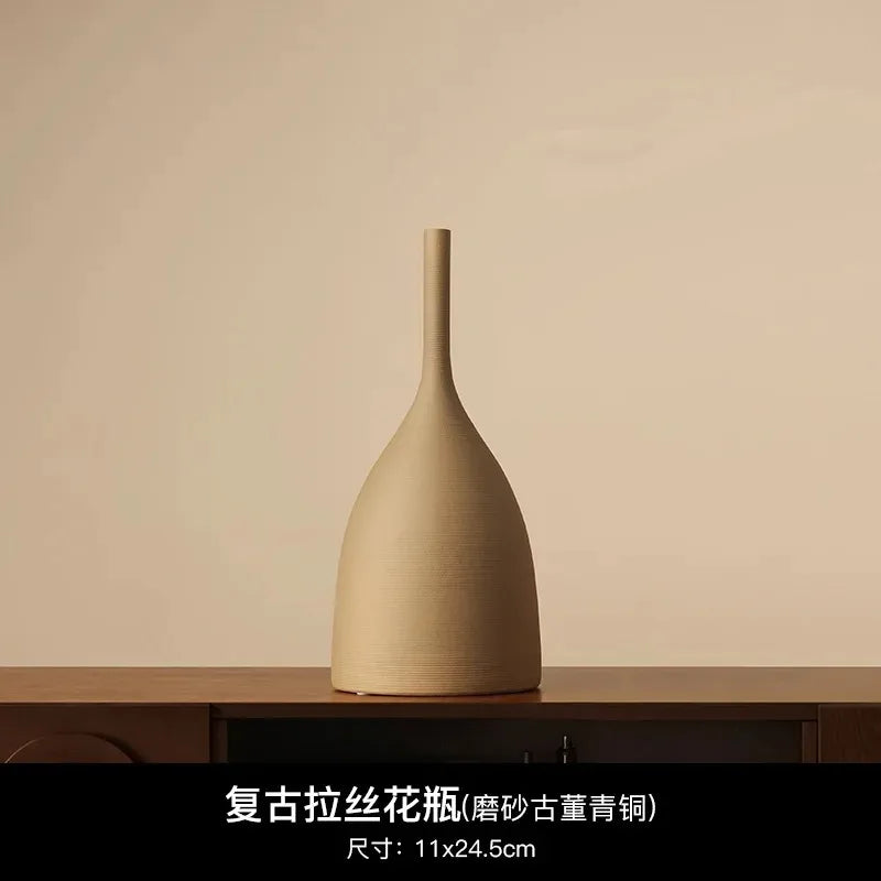 Minimalist beige ceramic vase with a textured matte finish, long slender neck, and rounded base on a wooden surface.