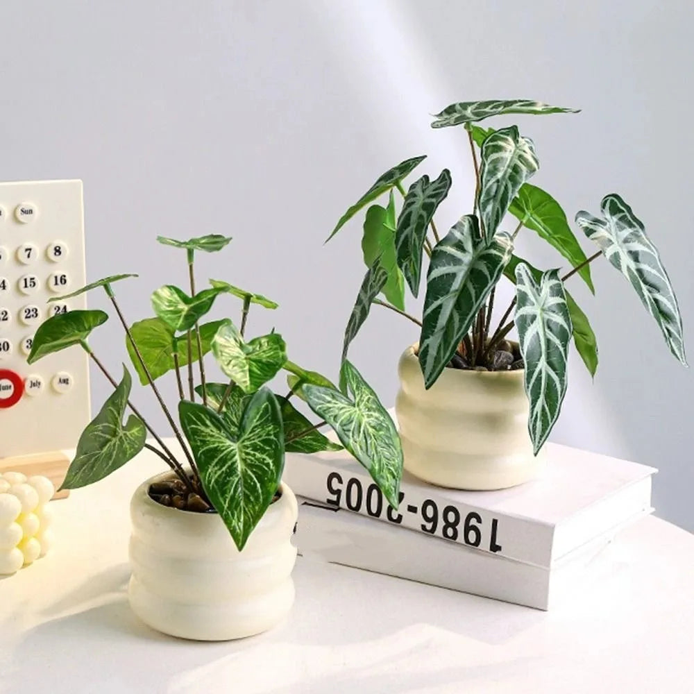 Two artificial plants with patterned green leaves in textured, cream-colored ceramic pots on a white table.