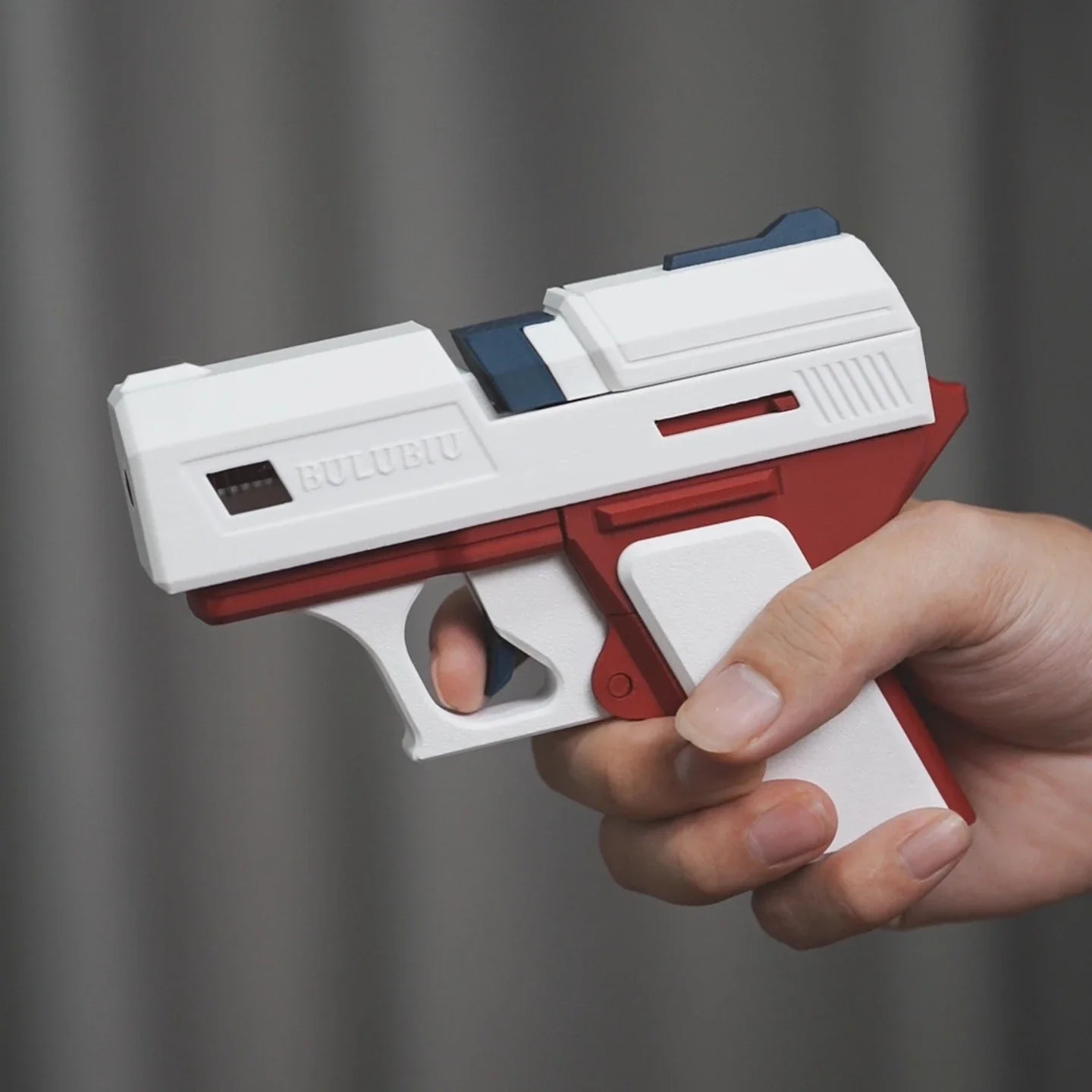 Hand holding a matte, white, red, and blue toy-style gun AirPods case. Hard plastic novelty design.