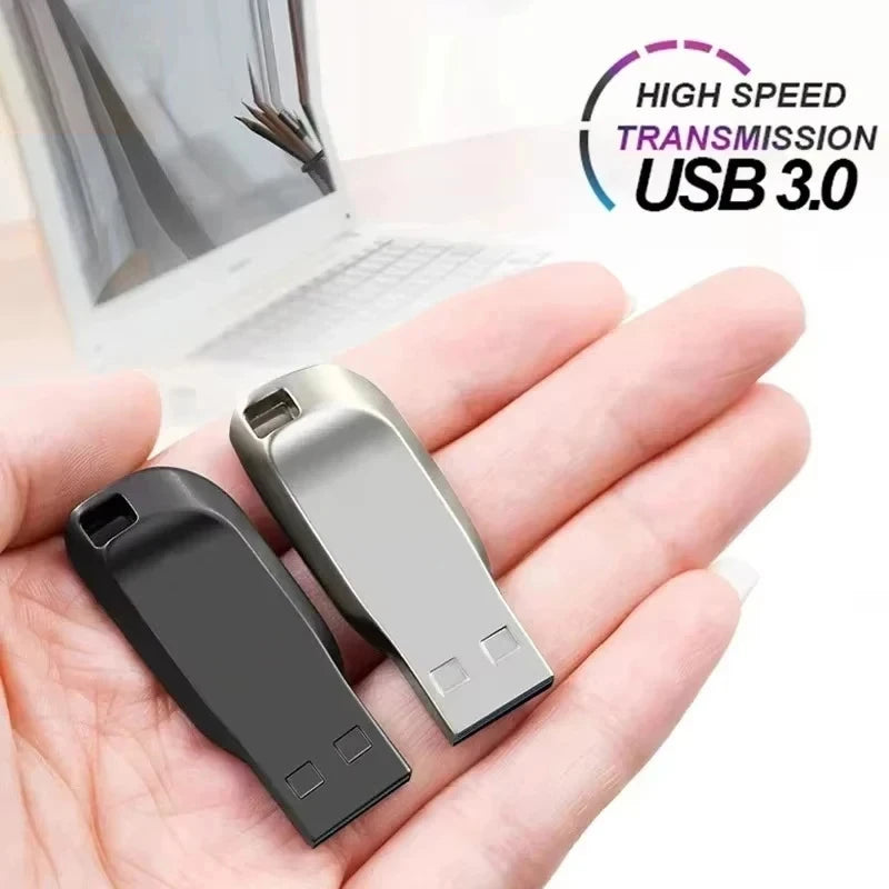 A hand holding two sleek, portable USB 3.0 flash drives in silver and black finishes, with a laptop in the background.