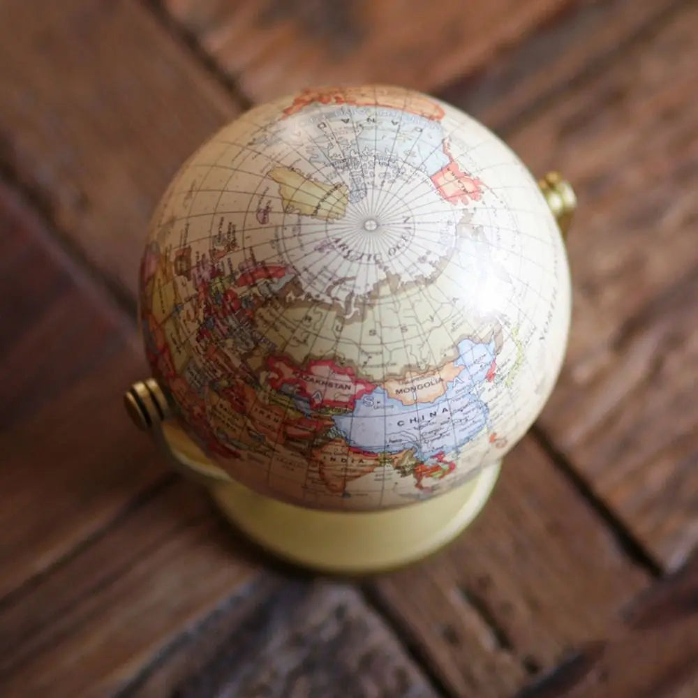 Cream-coloured vintage-style desk globe on a simple stand, showing world map details on a rustic wooden surface.
