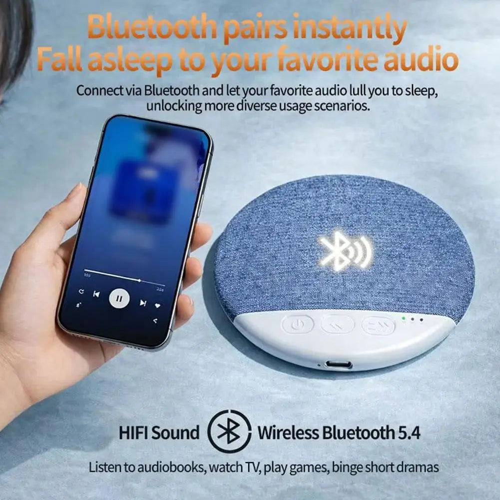 A round, blue fabric-covered wireless pillow speaker with white control buttons, shown connecting to a smartphone.