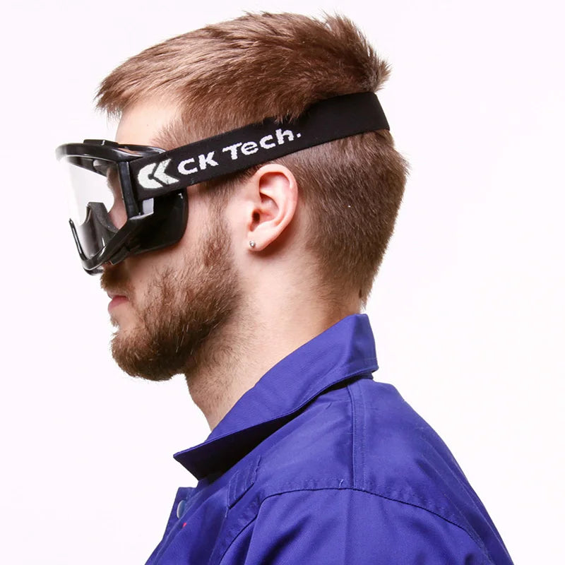 Profile of a man wearing black anti-impact safety goggles with clear lenses and a branded elastic strap.
