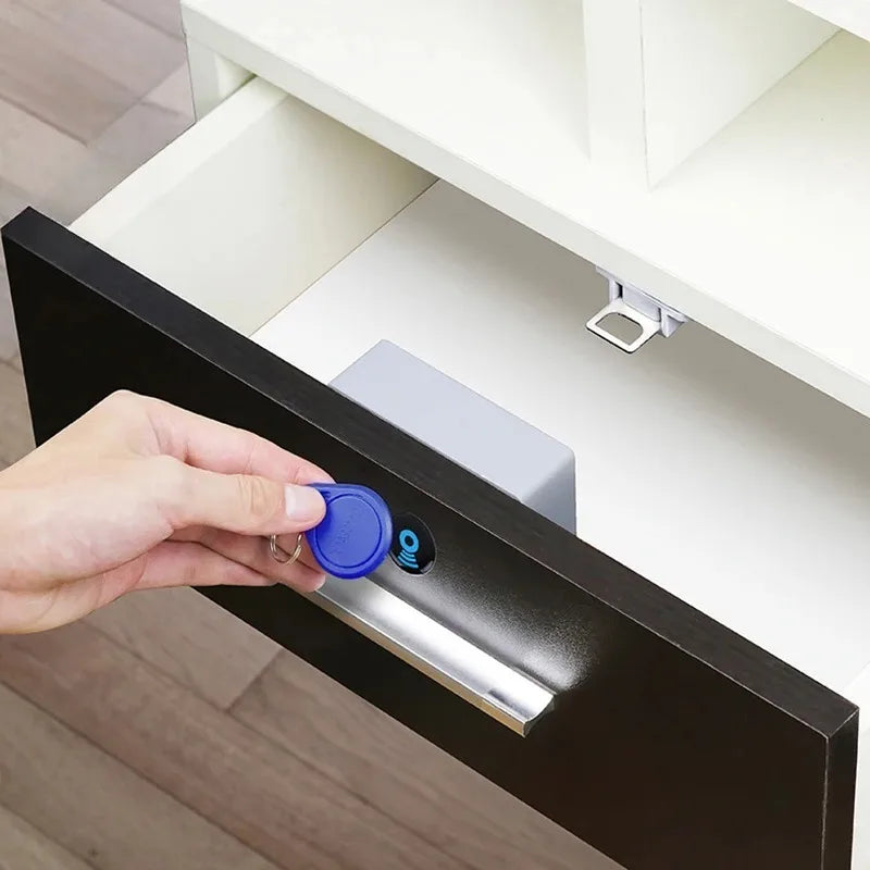 Grey plastic RFID drawer lock being unlocked with a blue key fob on a black wooden drawer.