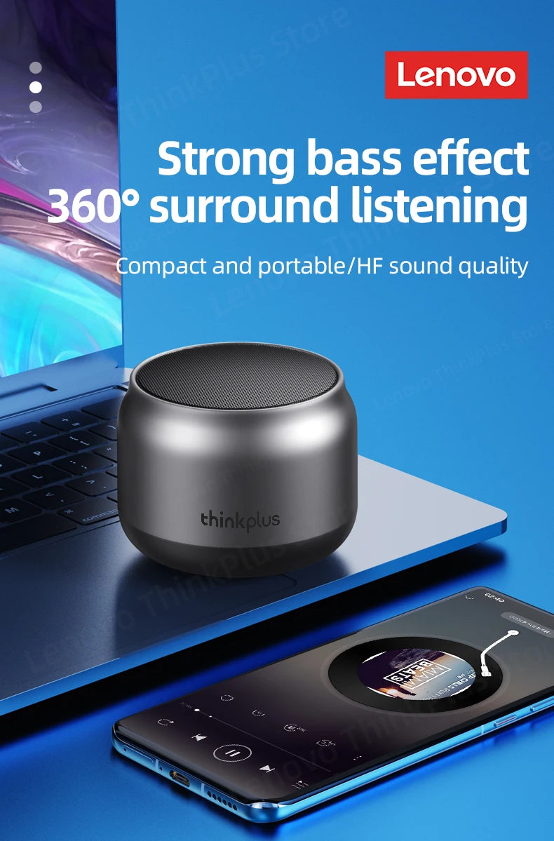A compact, grey, cylindrical Bluetooth speaker resting on a laptop next to a smartphone.