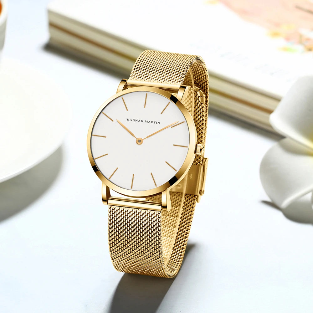 Minimalist gold women's watch with round white dial, thin markers, and mesh metal band.
