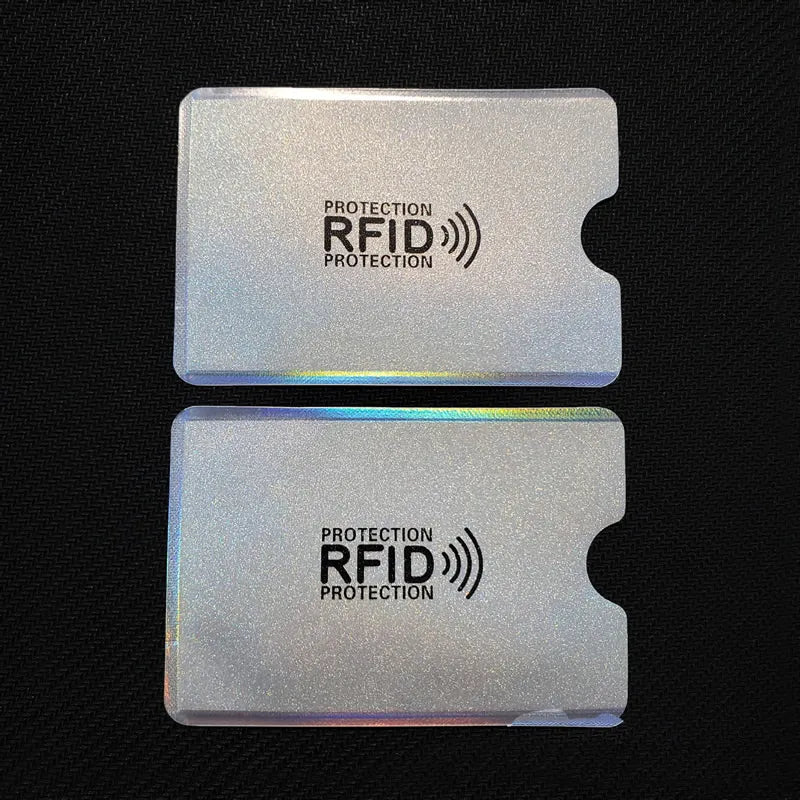 Two rectangular, silver, holographic RFID-blocking card sleeves with a thumb cutout, printed with black text and icon.